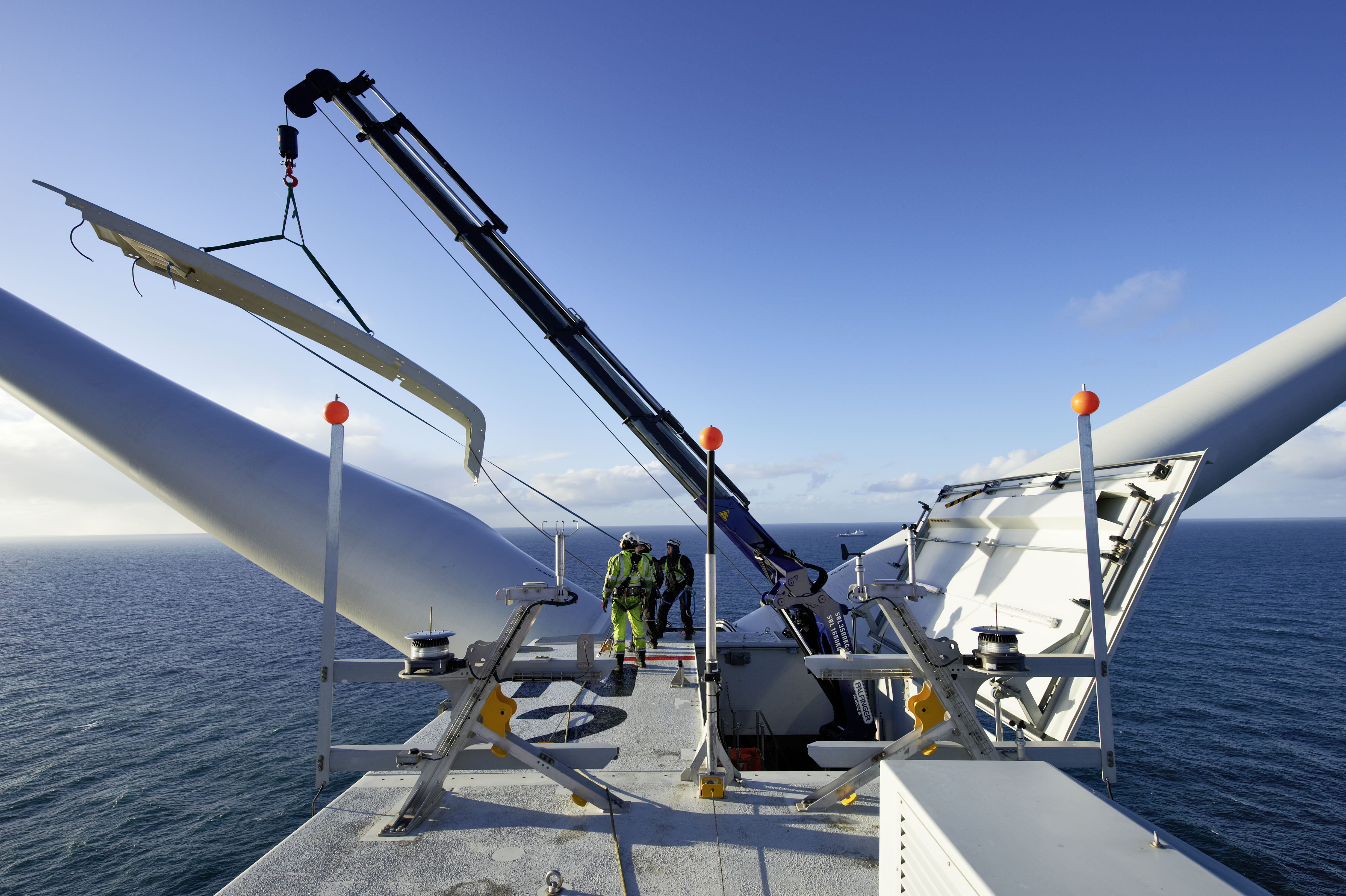 Engineers working on offshore wind turbine nacelle with ocean in background